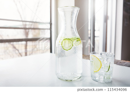 Glass, container and lemon water with cucumber in house for vitamin C, nutrition and healthy drink. Fruit, citrus and liquid with ice in jug on table for antioxidants, detox and organic hydration Glass, container and lemon water with cucumber in house for vitamin C, nutrition and healthy drink. Fruit, citrus and liquid with ice in jug on table for antioxidants, detox and organic hydration 115434096