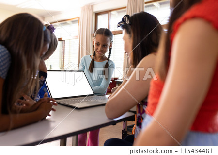 Group of children engaged with a laptop at a table in school, after class, with their teacher Group of children engaged with a laptop at a table in school, after class, with their teacher 115434481