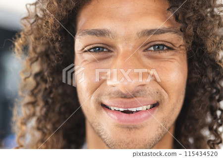 A young biracial man with curly hair smiles warmly at the camera 115434520