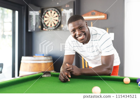 Young African American man smiles while leaning on a pool table 115434521