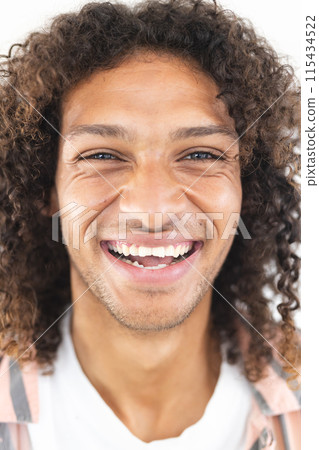 Young biracial man with curly hair smiles broadly, showcasing joy 115434522