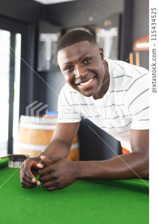 A young African American man smiles while leaning on a pool table 115434525
