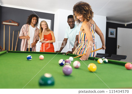 Diverse group of friends enjoys a game of pool, with a focus on a biracial woman taking her shot 115434570