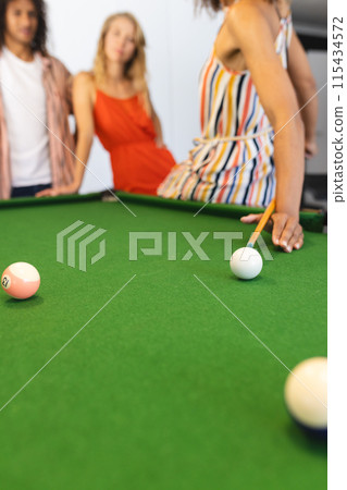 Focus is on a pool table with balls in a game setup, with a woman taking a shot 115434572