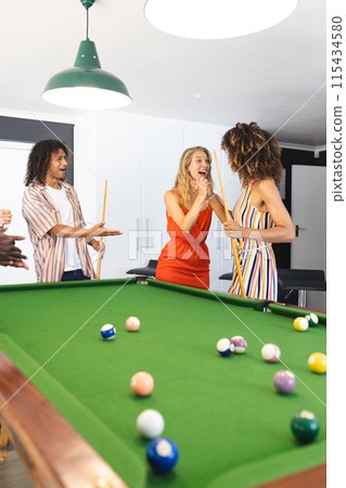Diverse group of friends enjoys a game of pool in a brightly lit room 115434580