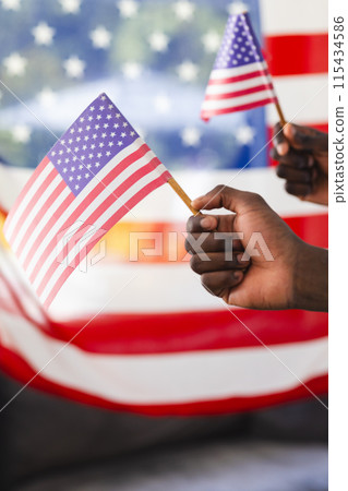 Two hands wave small American flags against a blurred background 115434586