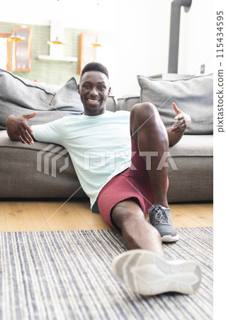 Young African American man in casual attire sits on the floor, smiling at the camera 115434595