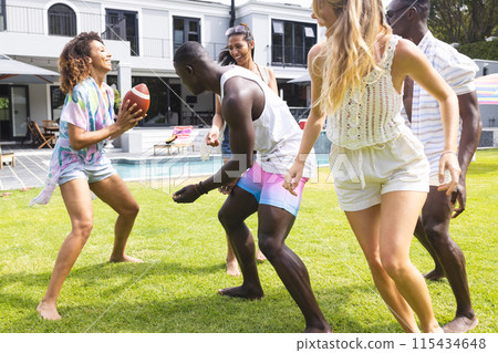 Diverse group of friends enjoy a playful game of football in a sunny backyard 115434648