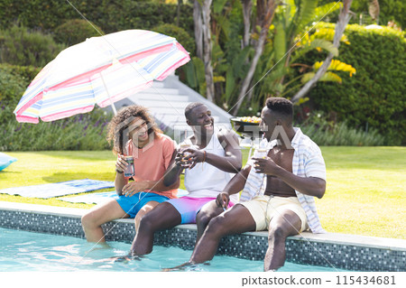 Three young men enjoy a sunny day by the pool, sharing laughter and drinks 115434681