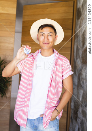 An Asian man holding a 'vote' badge proudly displays it 115434899