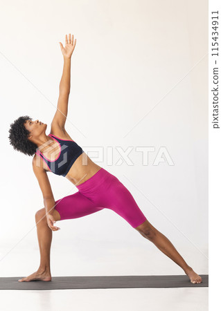 Biracial woman performs a yoga pose on a mat with copy space 115434911