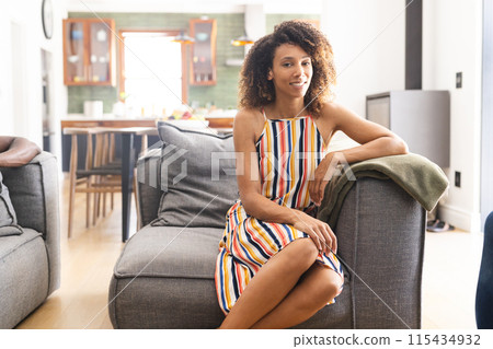 Biracial woman in a colorful striped dress sits relaxed on a grey sofa with copy space Biracial woman in a colorful striped dress sits relaxed on a grey sofa with copy space 115434932