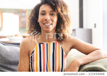 Biracial woman with curly brown hair smiles warmly, wearing a colorful striped top Biracial woman with curly brown hair smiles warmly, wearing a colorful striped top 115434948