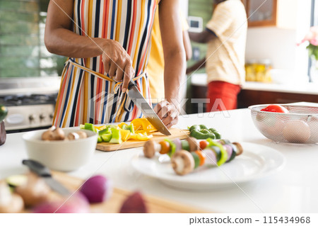 Biracial woman is chopping vegetables in a kitchen 115434968