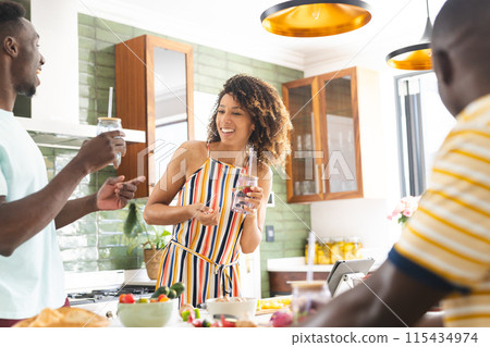 Diverse friends of young African American men and a biracial woman enjoy drinks in a sunny kitchen 115434974