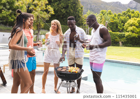 Diverse group of friends enjoys a barbecue by the pool, with mountains in the background Diverse group of friends enjoys a barbecue by the pool, with mountains in the background 115435001