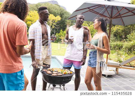 Diverse friends enjoy a barbecue outdoors, with a young African American man at the grill Diverse friends enjoy a barbecue outdoors, with a young African American man at the grill 115435028