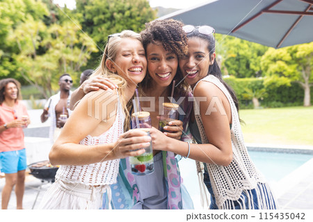 Three diverse female friends are embracing and smiling at an outdoor pool party 115435042