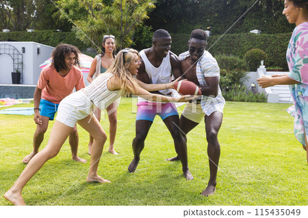 Diverse group of friends playing football in a sunny backyard, laughter evident 115435049