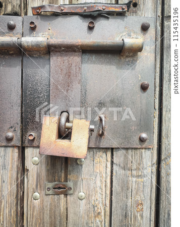 Texture of a wooden plank fence with vertical wood strips, brown wooden fence door with padlock Texture of a wooden plank fence with vertical wood strips, brown wooden fence door with padlock 115435196
