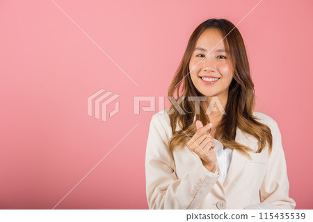 Confident business woman stands with a smile, creating a mini heart sign with her finger on a pink background. Asian portrait of a beautiful young female sending love for Valentine's Day, studio shot Confident business woman stands with a smile, creating a mini heart sign with her finger on a pink background. Asian portrait of a beautiful young female sending love for Valentine's Day, studio shot 115435539