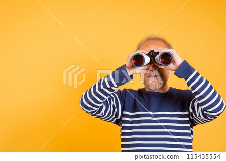 Portrait Asian smiling old man looking camera through binoculars studio shot isolated yellow background, senior man pensioner feeling surprised using binocular 115435554