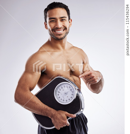 Portrait, happy and man pointing with scale for fitness in studio for body care, wellness, health or diet for muscles. Male person, athlete or dietitian and smile for weight loss by white background 115436294