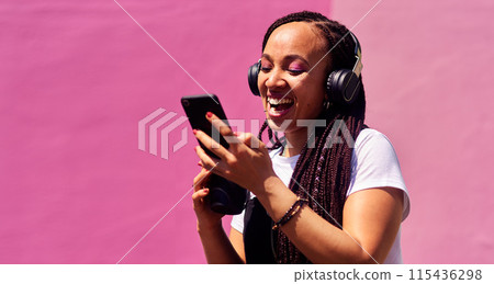 Woman, headphones and happy music for podcast in the city, pink wall background and audio on smartphone. Streaming, funny and female with coffee listening to track, singing on cellphone and excited 115436298