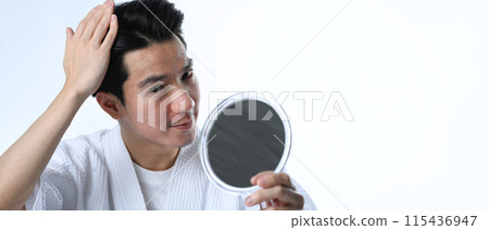 Young Asian man examining his hair while looking at the mirror isolated on white background Young Asian man examining his hair while looking at the mirror isolated on white background 115436947