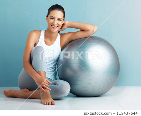 Fitness, happy woman and exercise ball in portrait on floor for core workout, balance and weight loss in studio. Smile and female person with training equipment for health with blue background 115437644