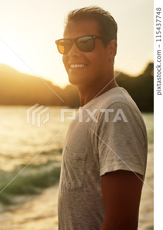 Man, sunglasses and happy on ocean for vacation, relax and summer break in nature for travel adventure. Sunset, seashore and smile outdoor for holiday, California and confident with tourist 115437748