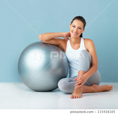 Fitness, happy woman and exercise ball in portrait on floor for core workout, balance and rest in studio. Smile and female person with training equipment for health, weight loss and blue background Fitness, happy woman and exercise ball in portrait on floor for core workout, balance and rest in studio. Smile and female person with training equipment for health, weight loss and blue background 115438105