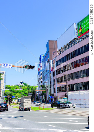 Kumamoto Castle stands out against the blue sky, and trams and road traffic run through the downtown area (Torimachi-suji, Kumamoto City) 115439056