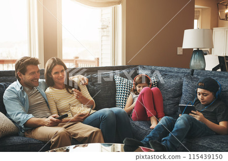 Family, children and parents in living room, watching tv or streaming on tablet with bonding on sofa. Mother, father and kids with electronics, popcorn or movies to relax with show on couch at house 115439150