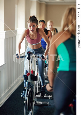 Woman, personal trainer and cycling with spin class at gym for cardio exercise or indoor workout. Female person, group or cyclists riding on equipment or bicycle with coach for fitness at health club 115439183
