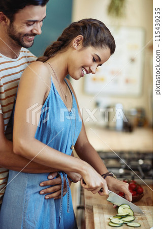 Man, woman and hug with smile for cooking in kitchen, care and diet with knife to prepare lunch in home. Indian people, happy couple and embrace with cucumber, love and meal prep for dinner in house 115439255