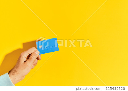 Male hand holds blue plastic bank card over yellow background with copy space Male hand holds blue plastic bank card over yellow background with copy space 115439520