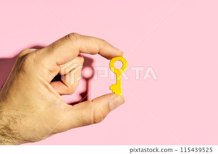 Man's hand holding yellow key against pink background Man's hand holding yellow key against pink background 115439525