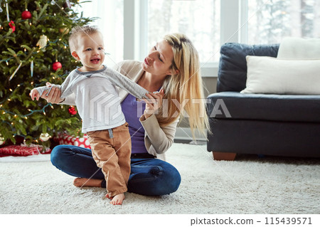 Mother, baby and happy while on floor in living room, holding hands for love and christmas holiday. Smile, motherhood and toddler with woman together, hug and play by sitting for relationship at home 115439571
