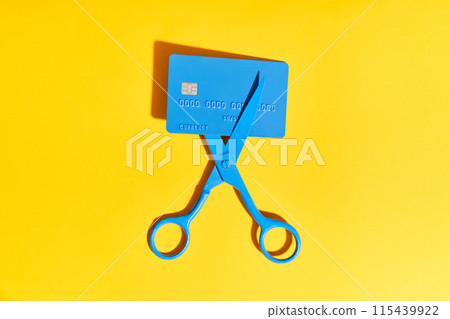 Blue scissors cutting credit card on yellow background Blue scissors cutting credit card on yellow background 115439922