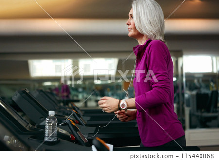 Senior woman, running on treadmill and training by music in gym club, water and bottle for health in wellness. Mature, female runner and exercise with podcast, hydration and workout by speed machine Senior woman, running on treadmill and training by music in gym club, water and bottle for health in wellness. Mature, female runner and exercise with podcast, hydration and workout by speed machine 115440068