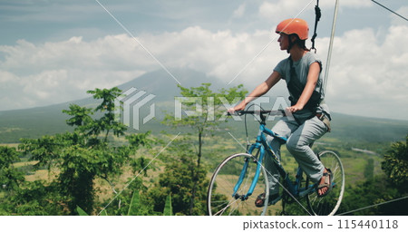 A womani riding a bike on top of a zip line over the beautiful volcanic crater lakes in the Philippines. The daring act combines biking and zip-lining for an adventurous experience. 115440118