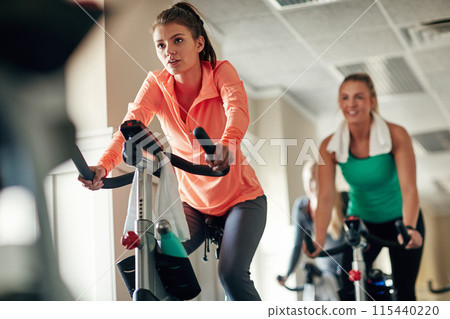Woman, cycling and workout with spin class for training, cardio exercise or indoor challenge at gym. Active female person or group of cyclists riding on equipment or bicycle in fitness at health club Woman, cycling and workout with spin class for training, cardio exercise or indoor challenge at gym. Active female person or group of cyclists riding on equipment or bicycle in fitness at health club 115440220