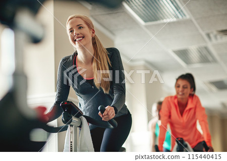 Women, exercise bike and class at gym, training and cycling for fitness or spinning studio. People, riding and stationary machine for workout challenge, aerobic instructor and equipment for cardio 115440415