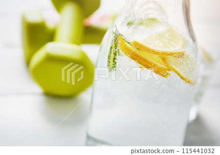 Jug, dumbbell and fitness with lemon water on table for detox, weight loss and healthy drink. Organic beverage, cucumber and container with citrus in liquid for vitamin C, antioxidants and nutrition 115441032