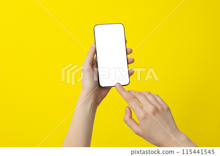 Female hand holding a smartphone on a yellow background Female hand holding a smartphone on a yellow background 115441545