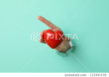 A female hand holds a red heart on a blue background A female hand holds a red heart on a blue background 115441576