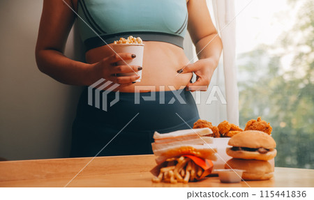 To eat or not. Cheerless plump woman looking at the burger while thinking to eat it or not 115441836
