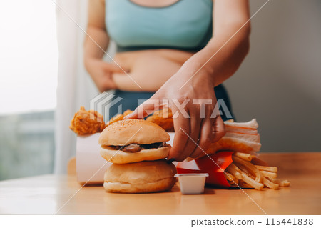 To eat or not. Cheerless plump woman looking at the burger while thinking to eat it or not To eat or not. Cheerless plump woman looking at the burger while thinking to eat it or not 115441838