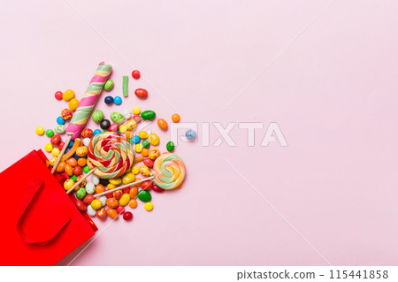 shopping paper gift bag in corner full of assorted traditional candies falling out on colored background with copy space. Happy Holidays sale concept shopping paper gift bag in corner full of assorted traditional candies falling out on colored background with copy space. Happy Holidays sale concept 115441858